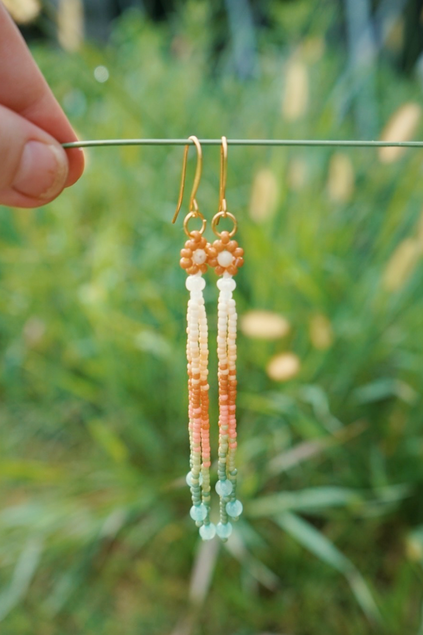 Beaded earrings hanging from a stick against a green grass backdrop