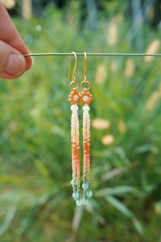 Beaded earrings hanging from a stick against a green grass backdrop