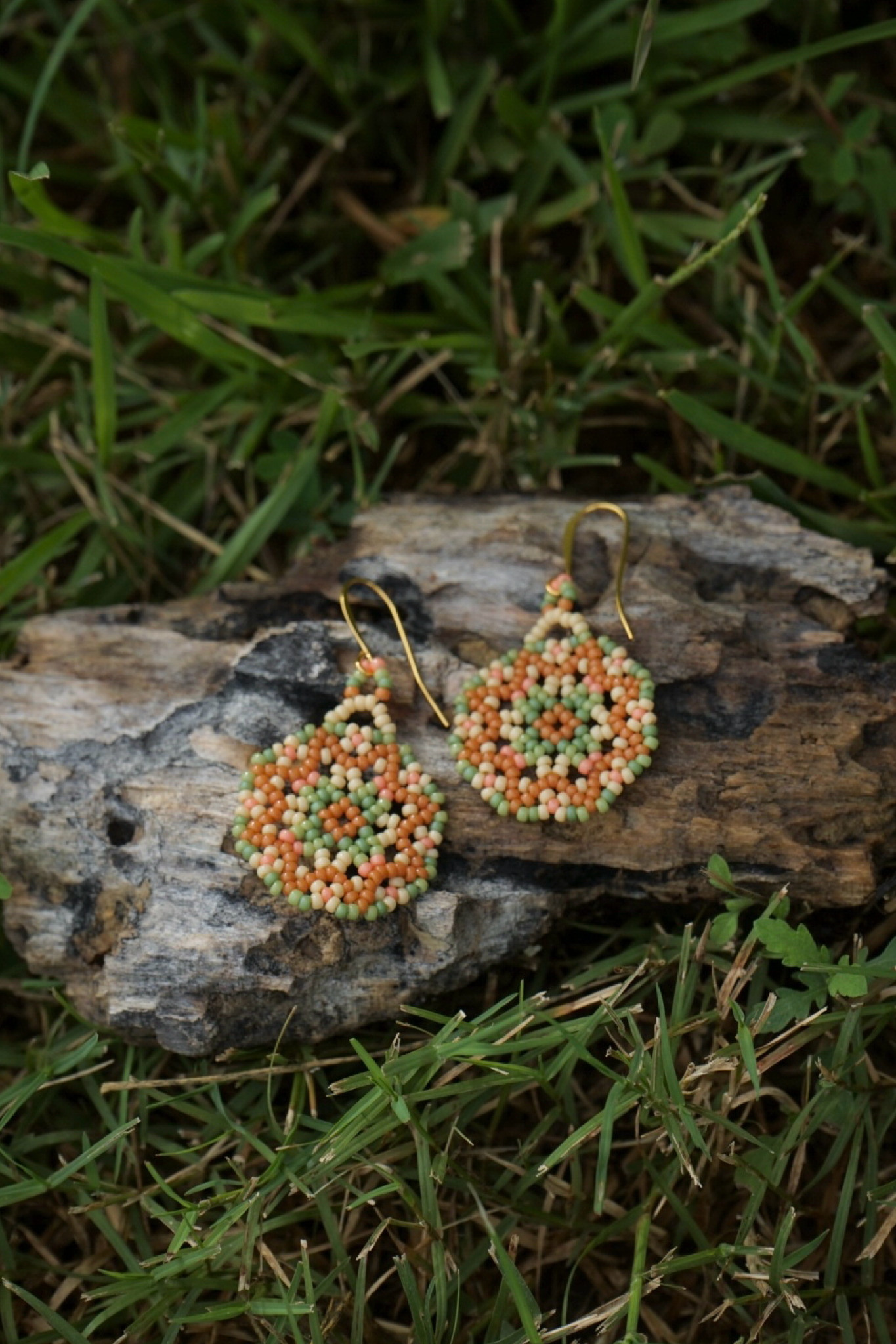 Beaded earrings on a wooden log with grass in the background