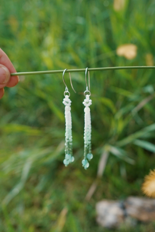 Green beaded earrings held on a grass stem with a blurred green background