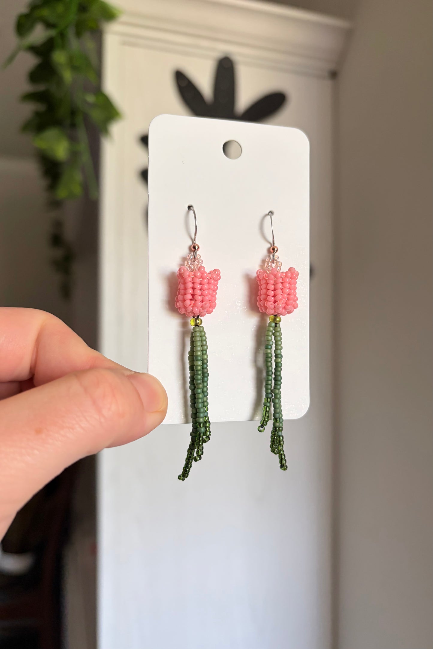 Pair of pink and green beaded earrings on a white card held by a hand.