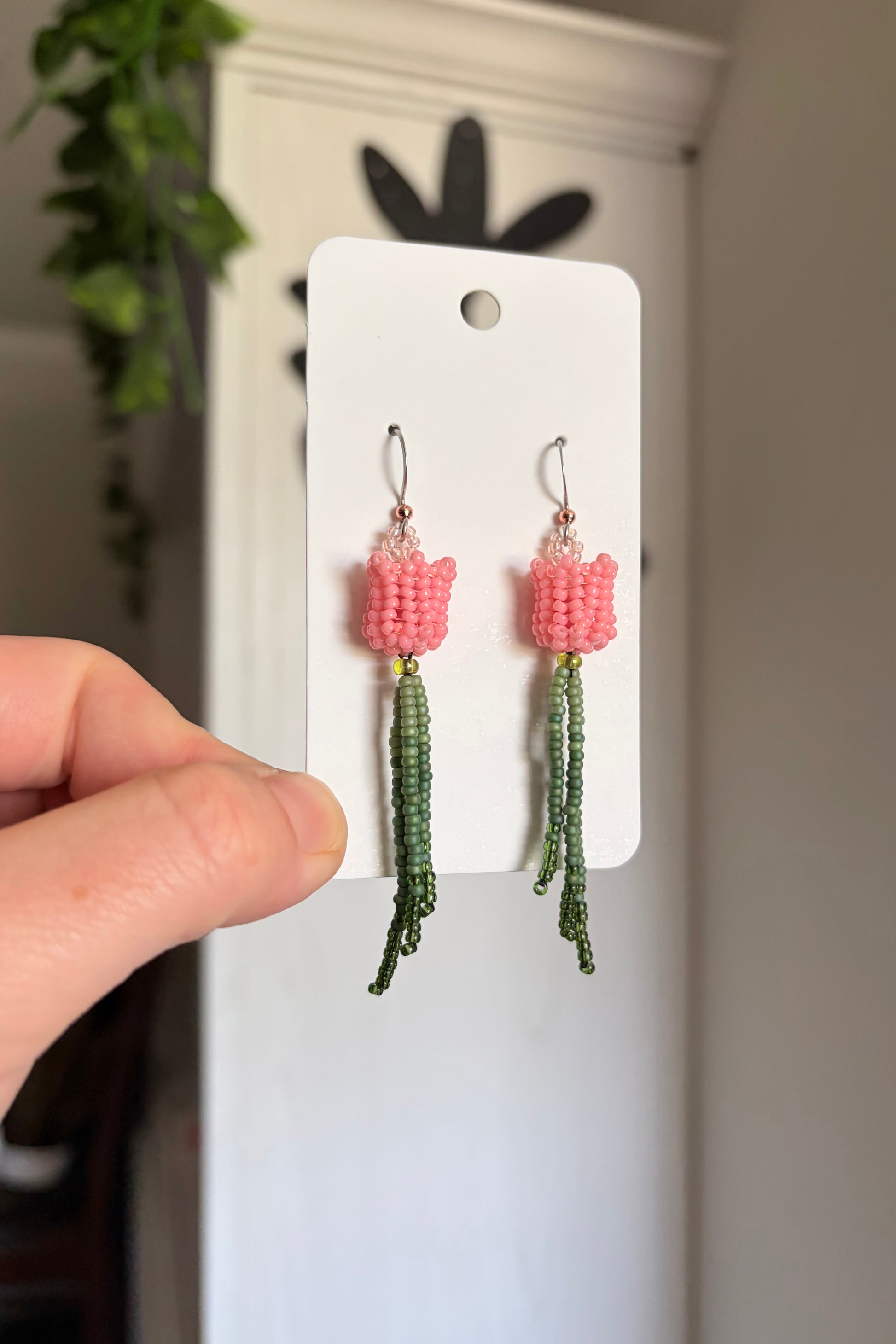 Pair of pink and green beaded earrings on a white card held by a hand.