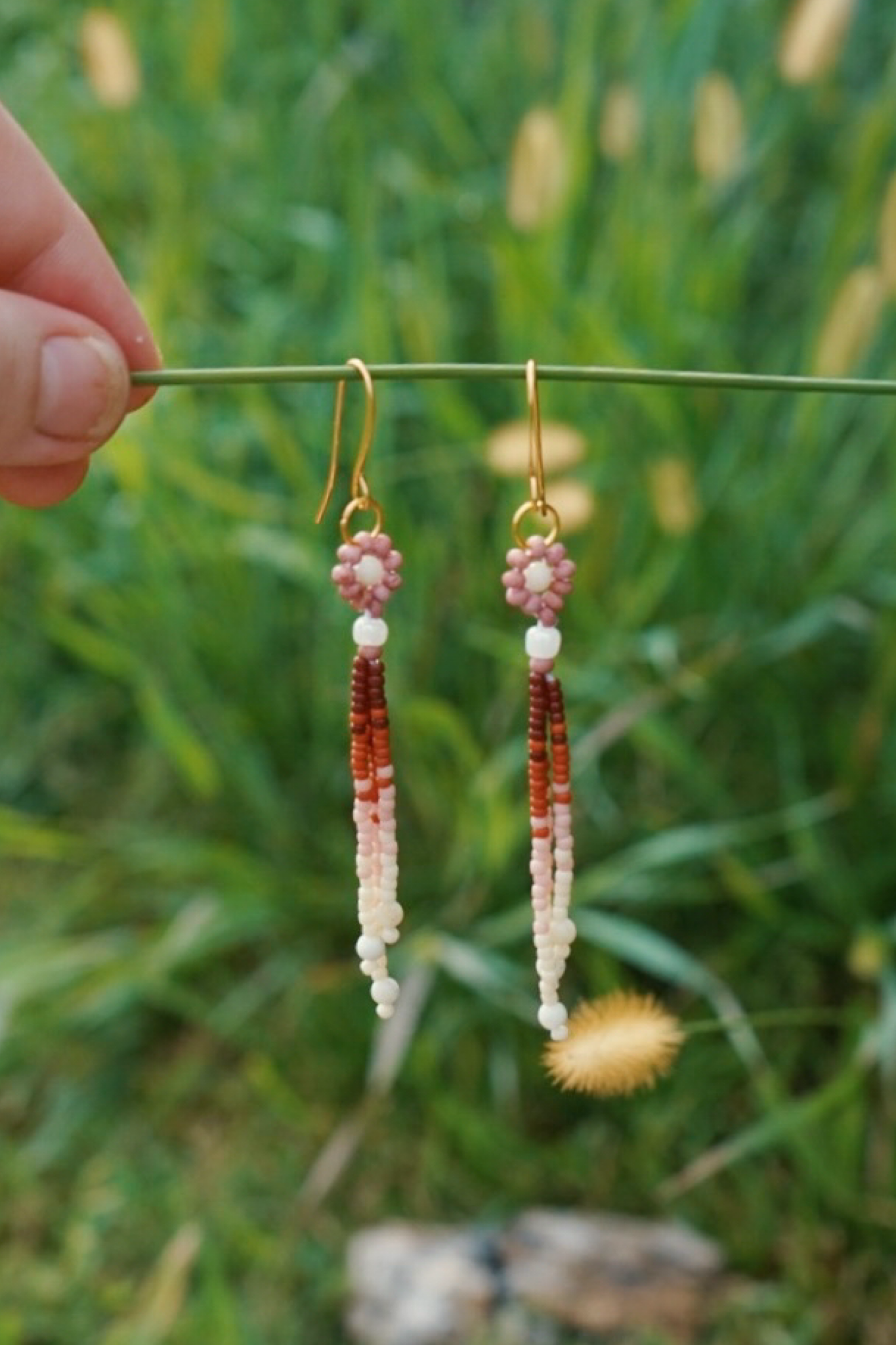 Pair of beaded earrings hanging from a stick against a grassy background