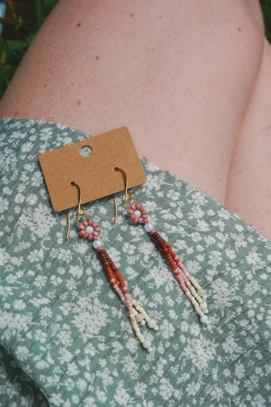 Beaded earrings on a cardboard display card against a floral-patterned fabric background