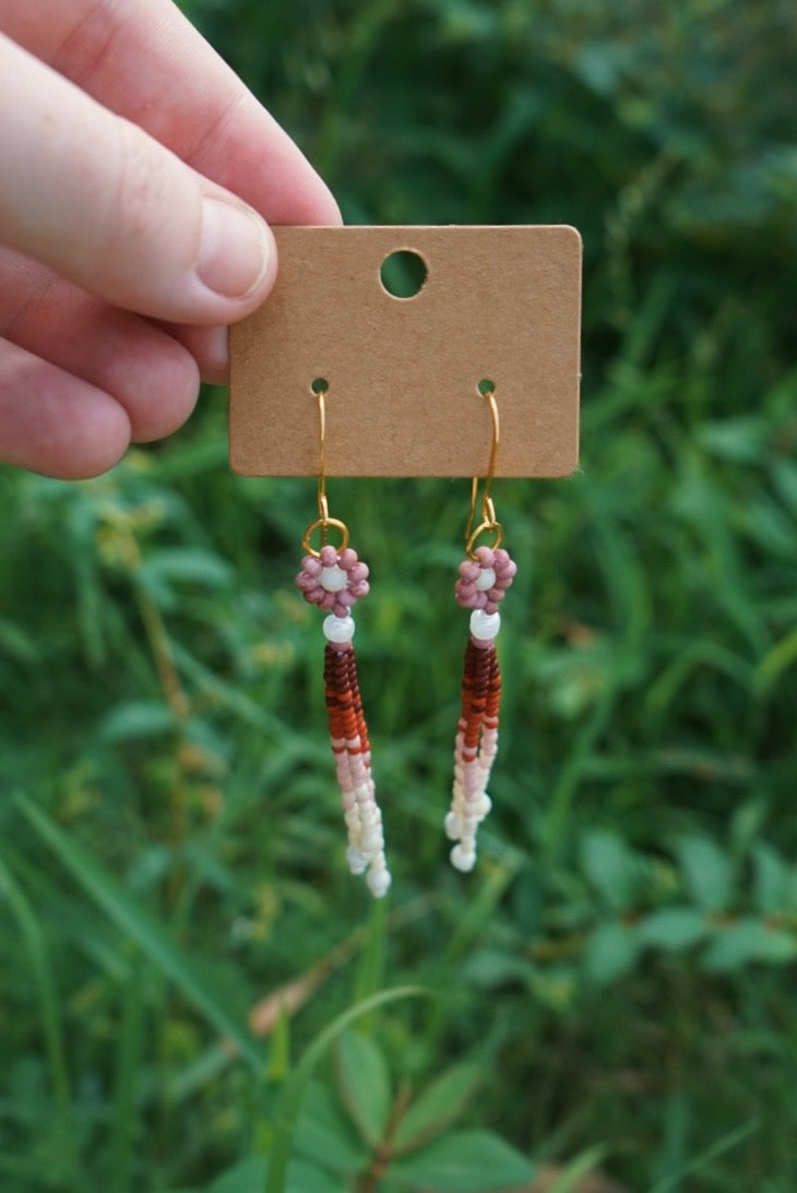 Hand holding a card with beaded earrings against a green leafy background