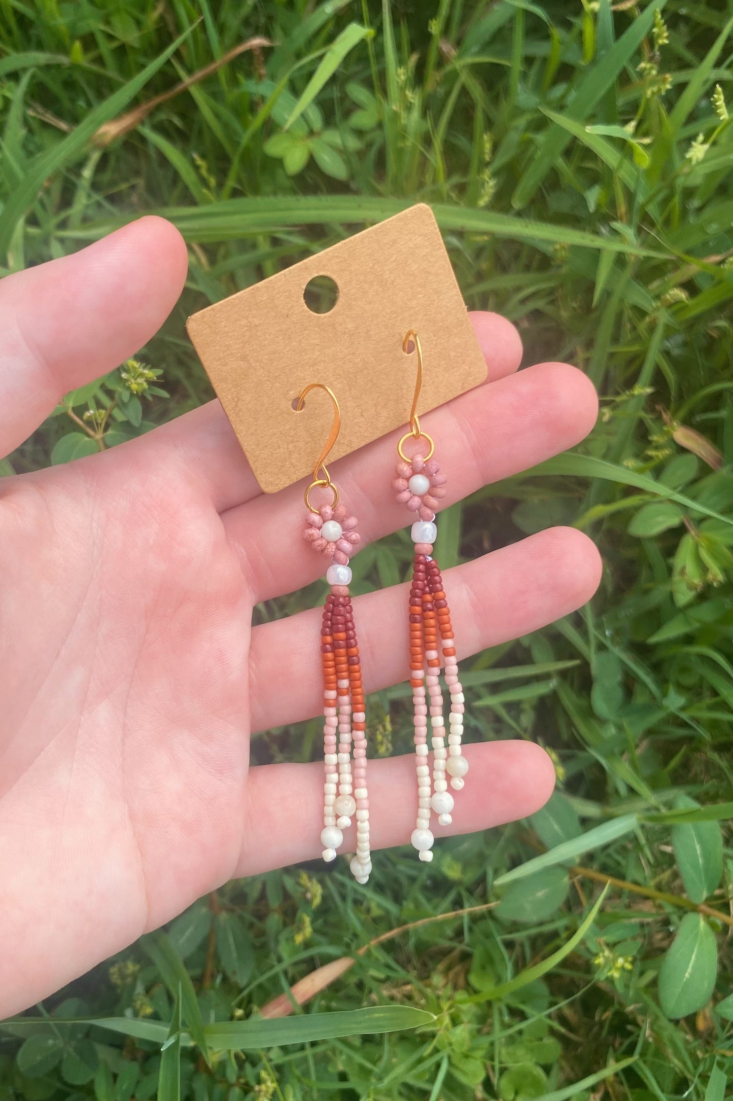 Beaded earrings on a card held in front of green grass